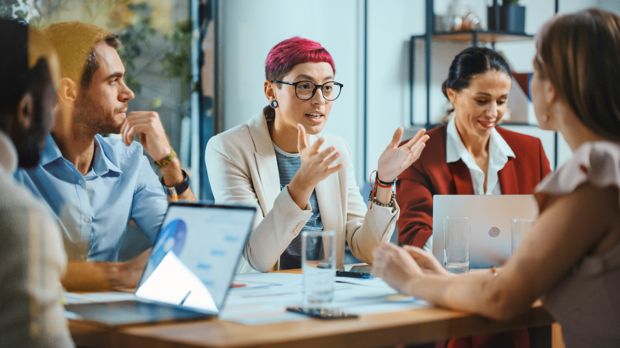 Persönlichkeitsanalyse «INSIGHTS MDI®» - Mitarbeiterin mit pinken Haaren und Brille sprich mit Gesten während eines Meetings